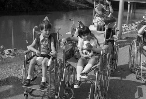 children seated in wheelchairs and wearing party favors alongside the Trinity River