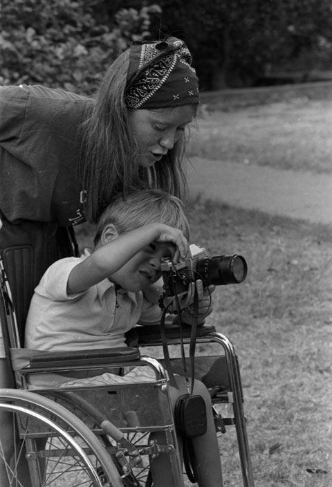 Volunteer helps a child in a wheelchair take a photograph