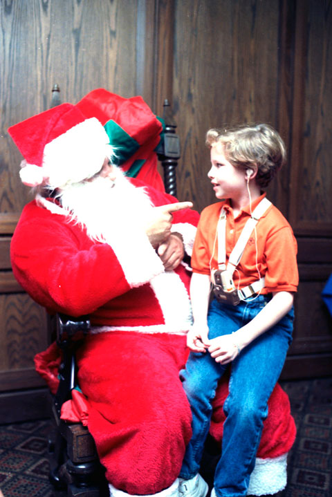 boy with listening device sits on a signing Santa's lap