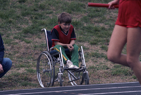 Young boy in wheelchair watches activities along the sidelines at the Special Olympics Games