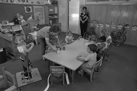 toddlers sitting around a short table with two adults in the classroom