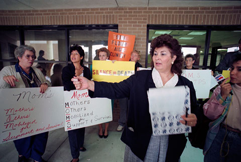 Women are holding signs that say, "MOM'S: Mother's Others Mobilizied for Support and Survival"
