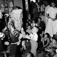 man dressed as Santa Claus presents a present to Charles Maclin while several children and adults look on