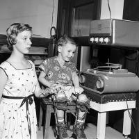 girl wearing an arm brace, and boy sitting, wearing leg braces, inspect a high fidelity music system