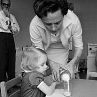 child receives assistance pouring milk from volunteer at rehabilitation center
