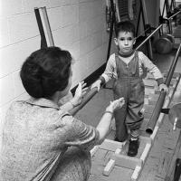 young patient assisted by volunteer enjoys a parallel bar exercise-game