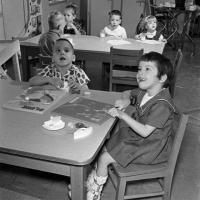 children play with puzzles at a table in a rehabilitation center; children behind them are having a glass of milk