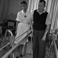 woman assists patient to walk with the help of parallel bars