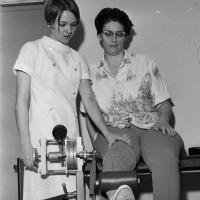 physical therapist assists woman on machine designed to strenghten leg muscles