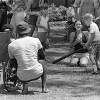 Children, including one in a wheelchair, playing baseball with adults assisting
