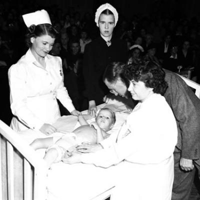 young polio patient in hospital bed surrounded by two women, doctor, and doctor's assistant