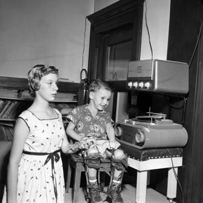 girl wearing an arm brace, and boy sitting, wearing leg braces, inspect a high fidelity music system