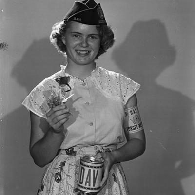 Louise Davis wearing a veterans cap and an armband holding a donation can and forget-me-not flowers