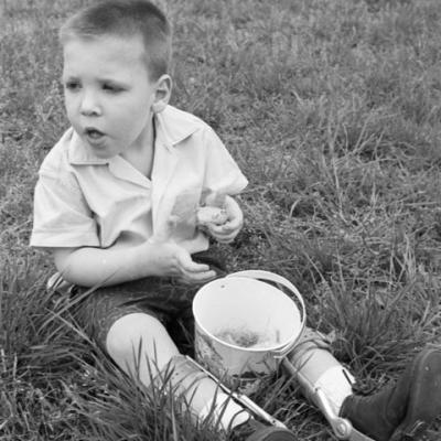 child in leg braces sits on lawn with an Easter basket