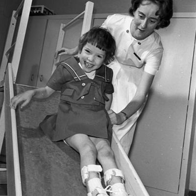 Girl enjoys a slide with physical therapist assisting 