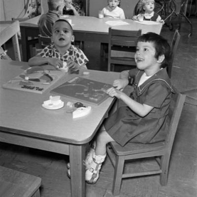 children play with puzzles at a table in a rehabilitation center; children behind them are having a glass of milk