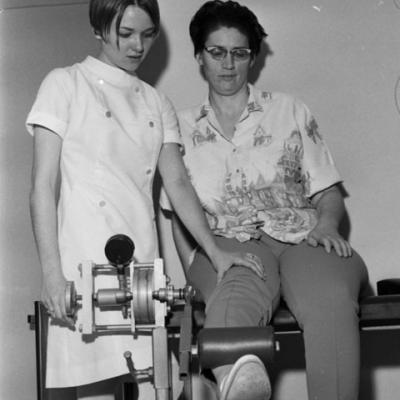 physical therapist assists woman on machine designed to strenghten leg muscles