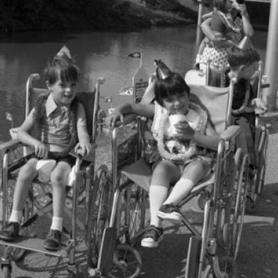 children seated in wheelchairs and wearing party favors alongside the Trinity River