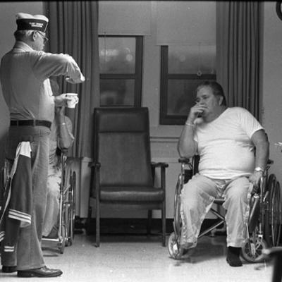 man sitting in a wheelchair and smoking a cigarette while listening to another man talk