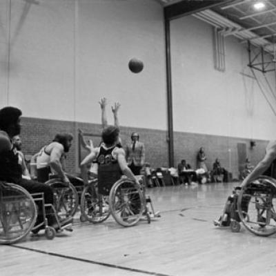 college students play wheelchair basketball in a high school gymnasium