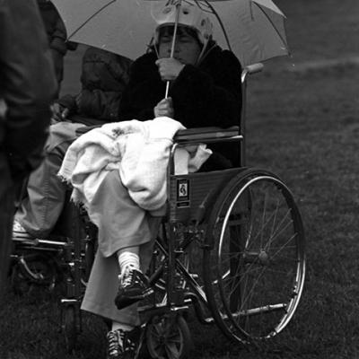 Special Olympics participant in wheelchair holding unbrella, waiting in rain