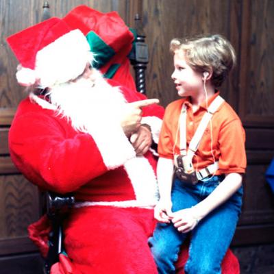 boy with listening device sits on a signing Santa's lap