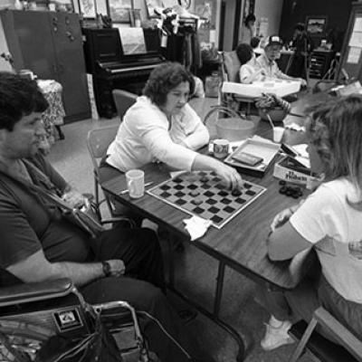 2 women playing checkers while a man in a wheelchair watches