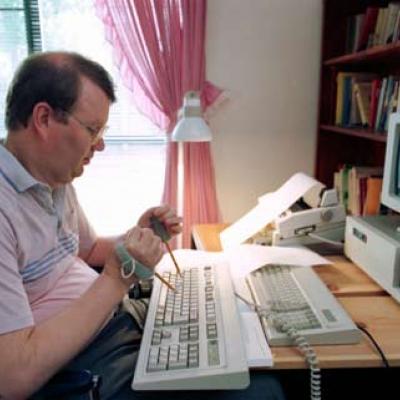 man using hand devices with pencils attached to type on a computer keyboard