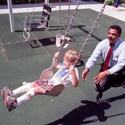 T.Ware, physical therapist, plays with Jeremy Burleson, age 4, on swing set designed for different levels of disability