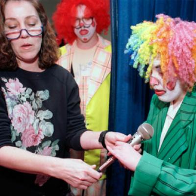  instructor Liz LaRochelle hands microphone to Erin Hendrix dressed as a clown