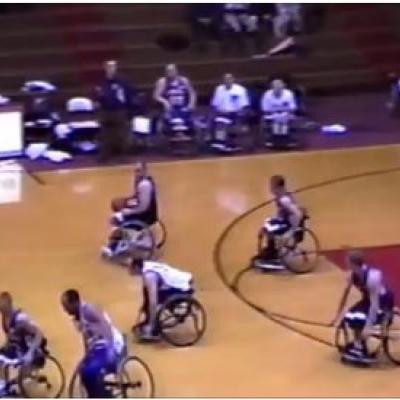 6 men in wheelchairs playing basketball and 4 people on sideline